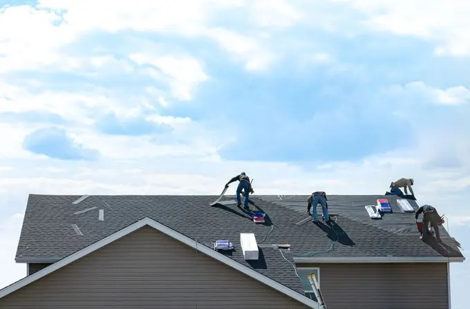 Roofing crew working on a house roof under a bright sky