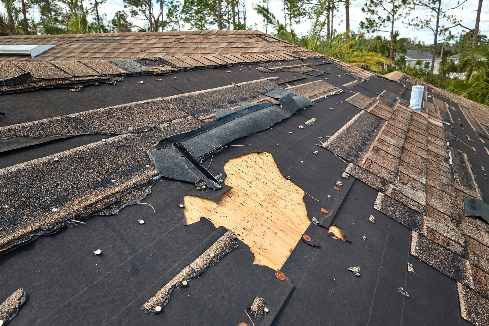 Storm-damaged roof with missing shingles exposing underlayment