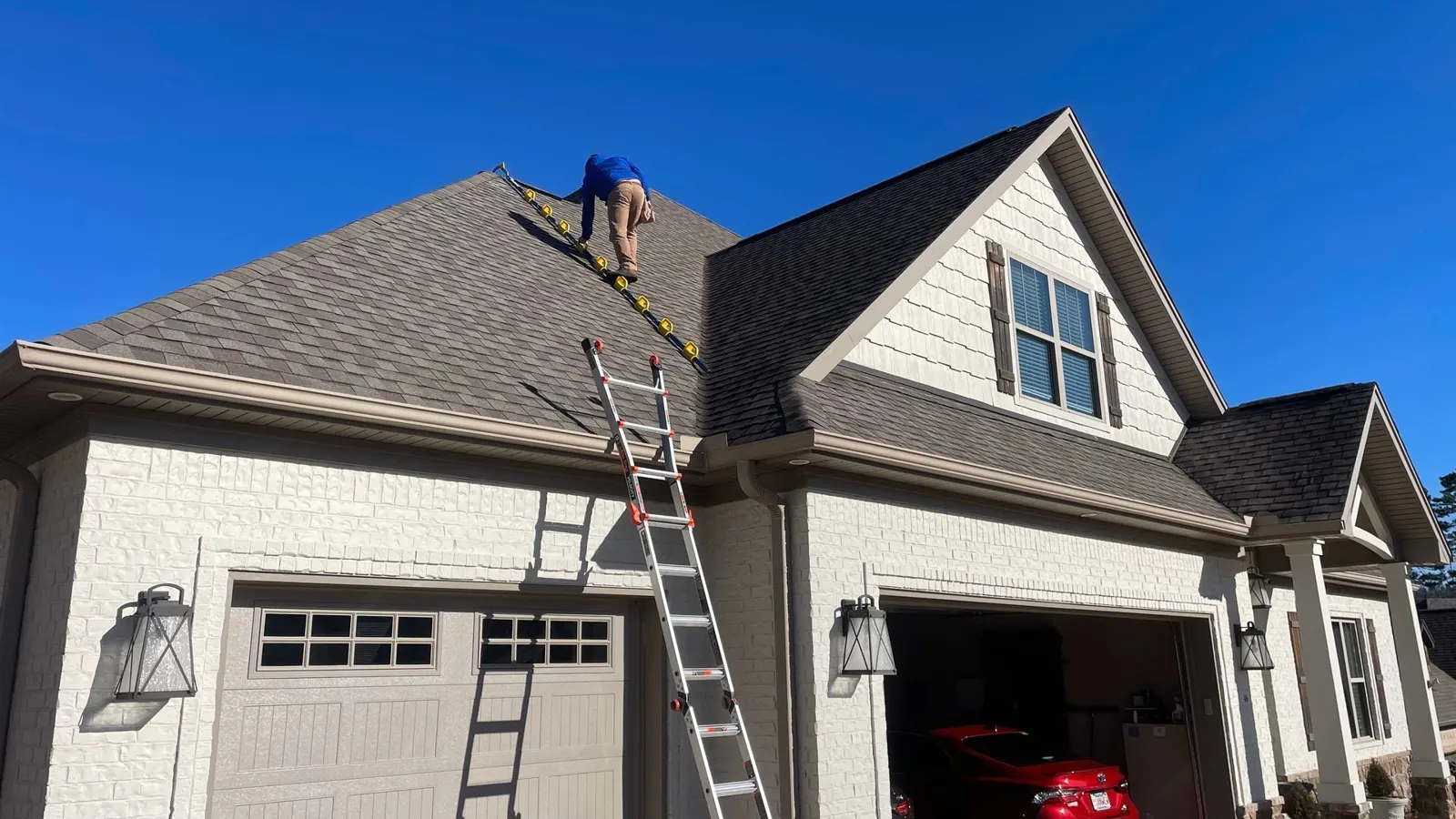 Roofer on a ladder inspecting a home’s roof under a blue sky