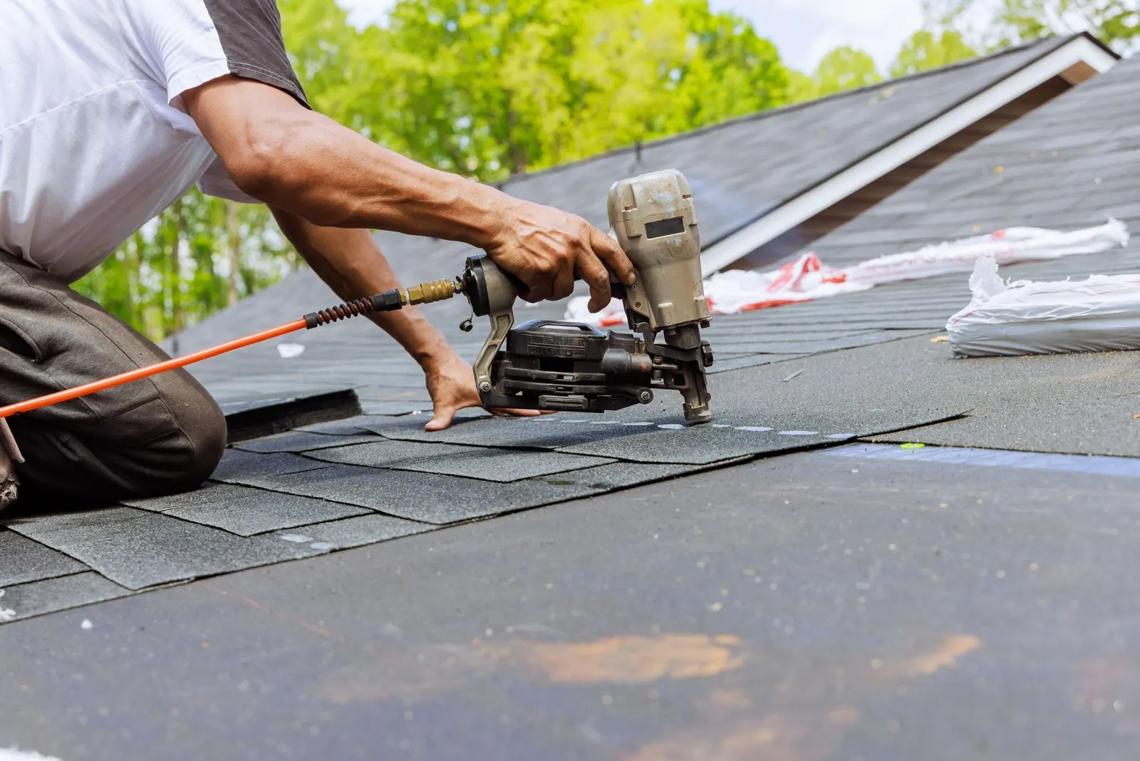 Roofer using a nail gun to install asphalt shingles