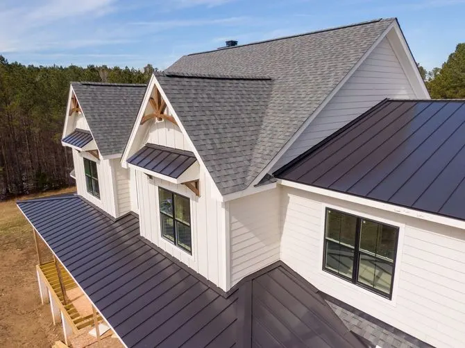 White house with black metal and gray shingle roofs and dormers